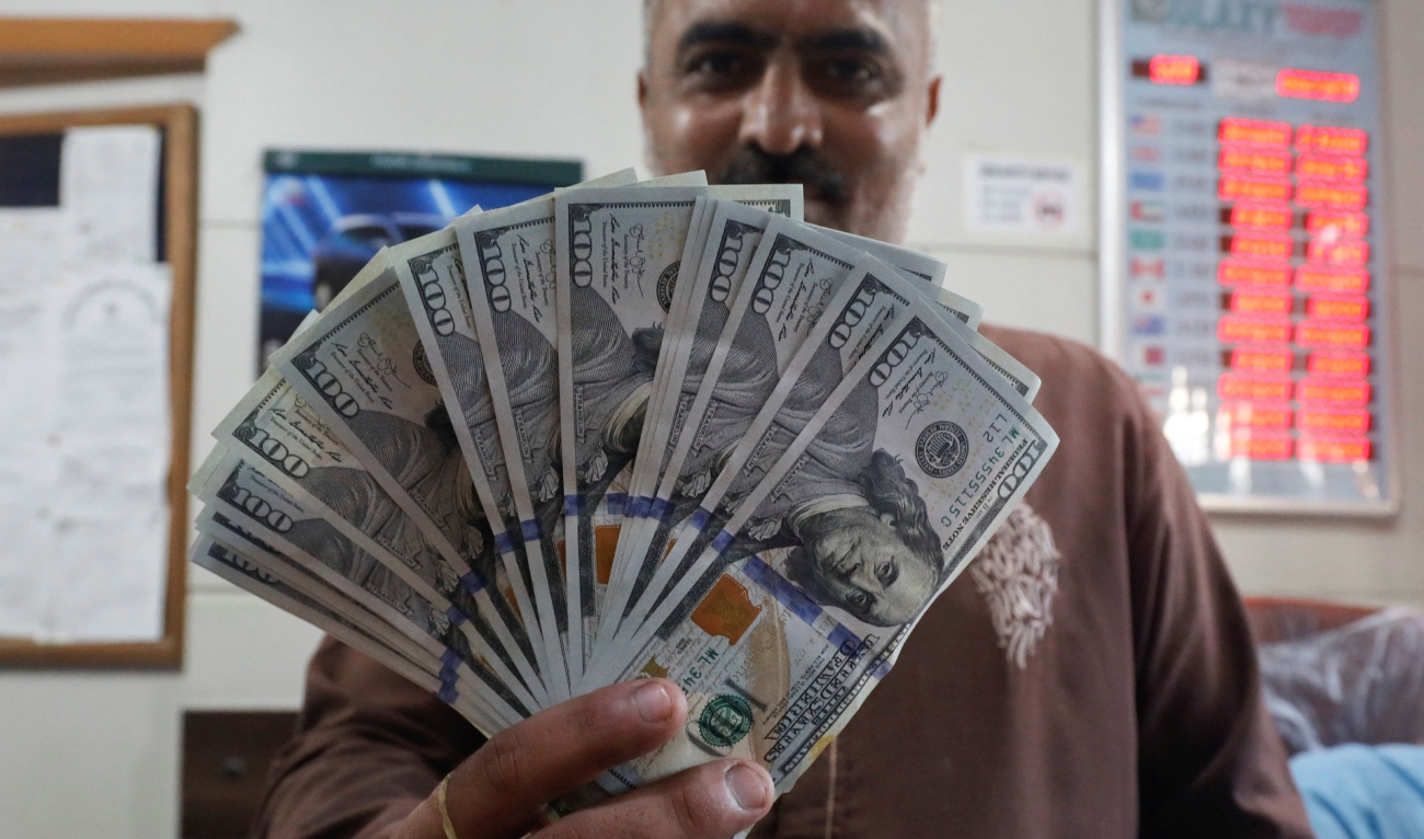 An employee of a foreign exchange shop poses with U.S. dollar banknotes from behind a glass booth in Karachi, Pakistan on September 7, 2023. (Photo courtesy: REUTERS)