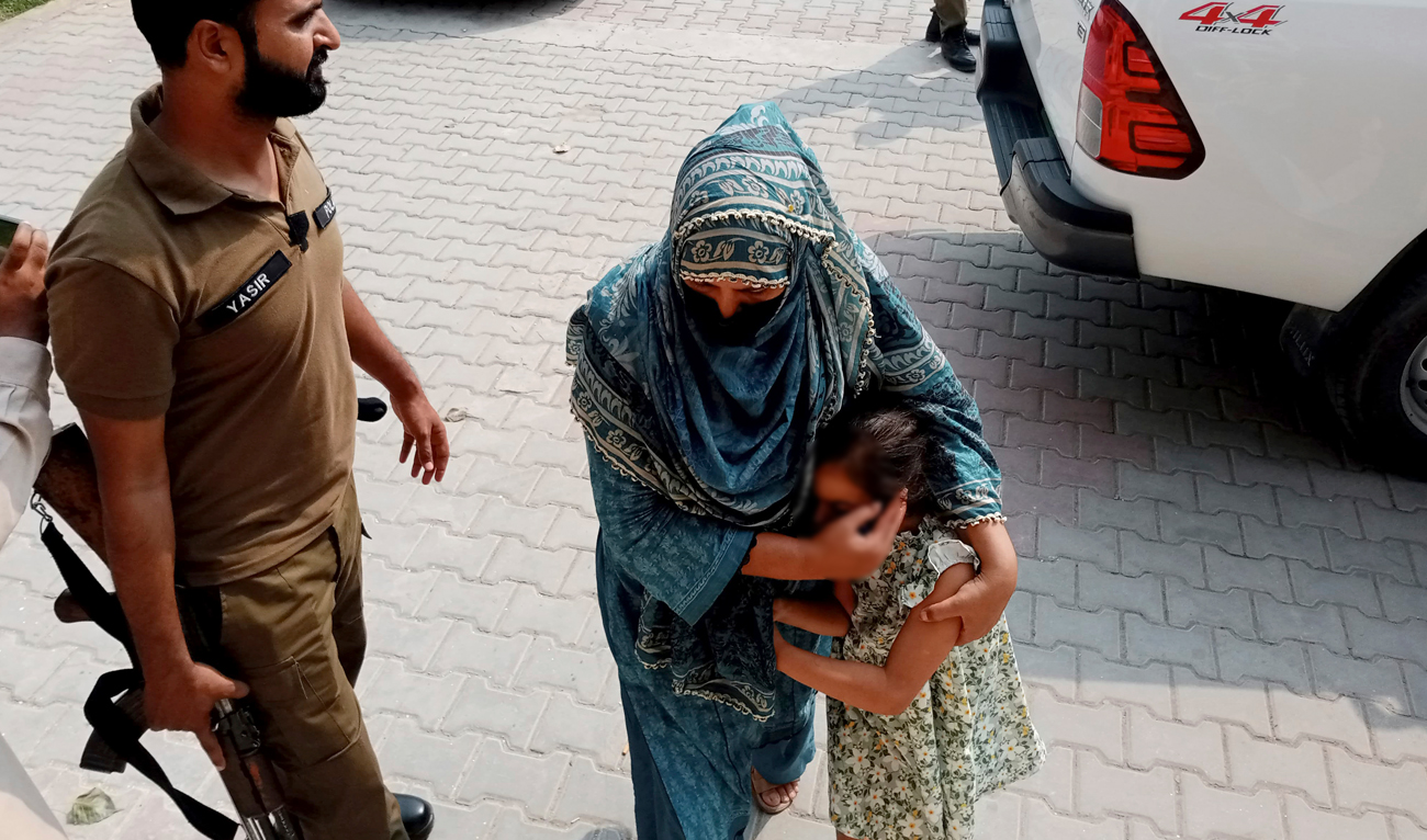 Police officers escort a relative and a child of a couple wanted by British police in connection with last month's death of their 10-year-old daughter on the outskirts of London, to appear them in a court in Jhelum, about 175 kilometres (110 miles) northwest of Lahore in central Pakistan on September 12, 2023. (AP)