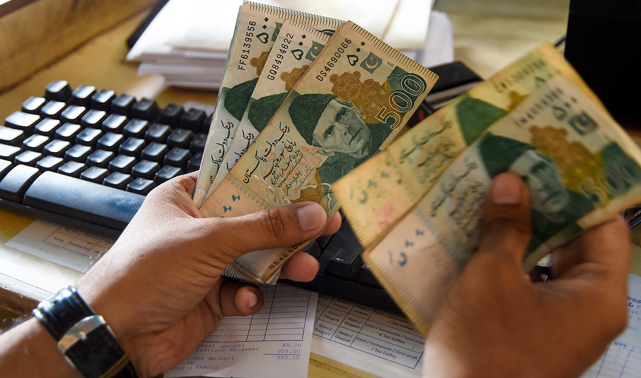 In this file photo, taken on May 16, 2019, a Pakistani man counts local currency at his shop in Karachi. (AFP/File)