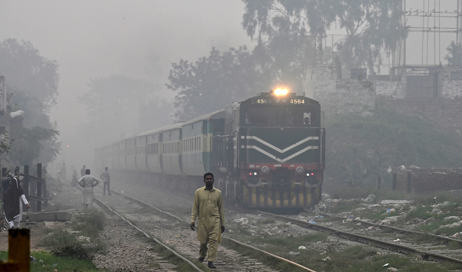 Commuters make their way along the railway tracks amid smoggy conditions in Lahore, Pakistan on November 7, 2023. (FP)