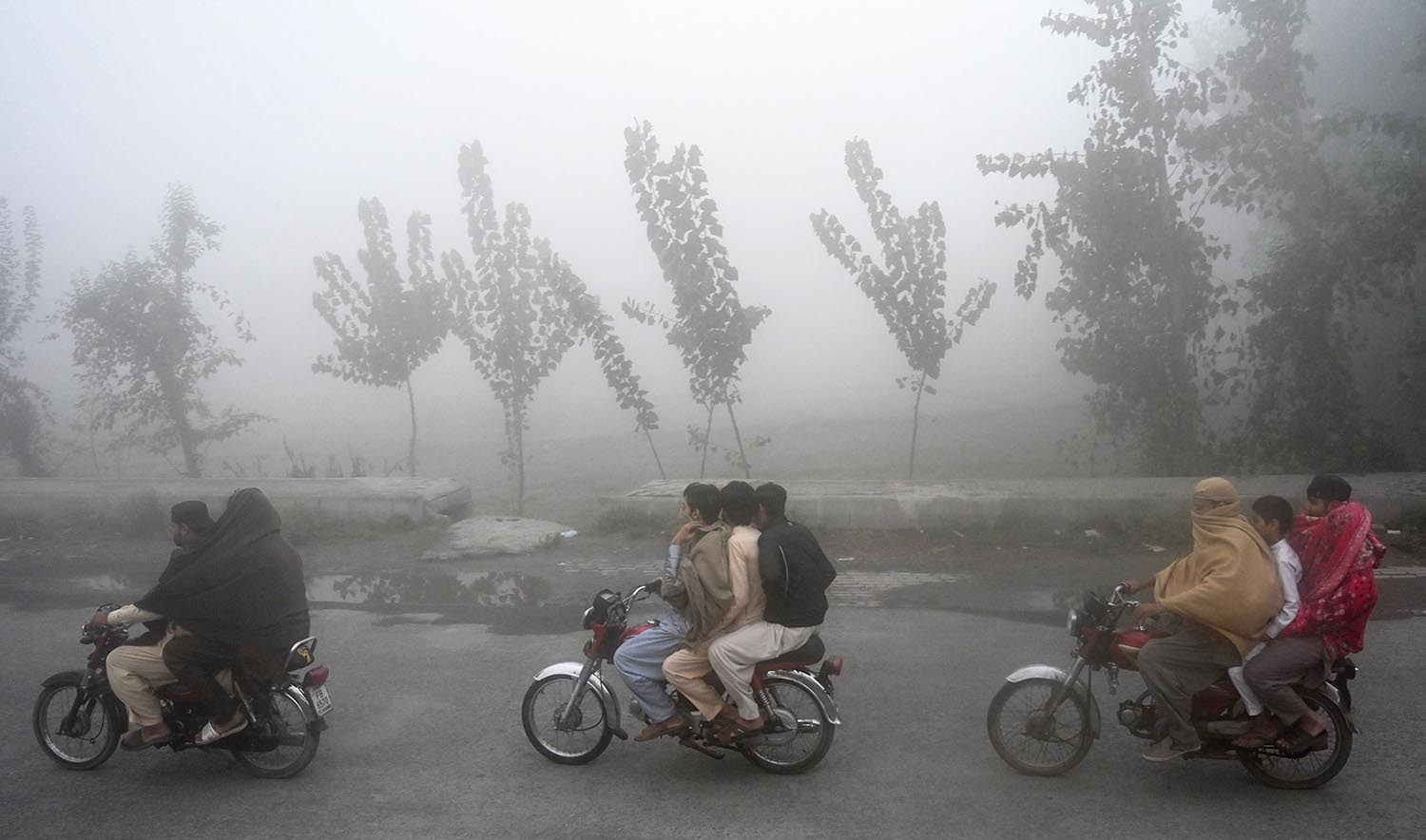 Men ride on bikes along a street amid smog conditions in Peshawar on November 11, 2023. (AFP)