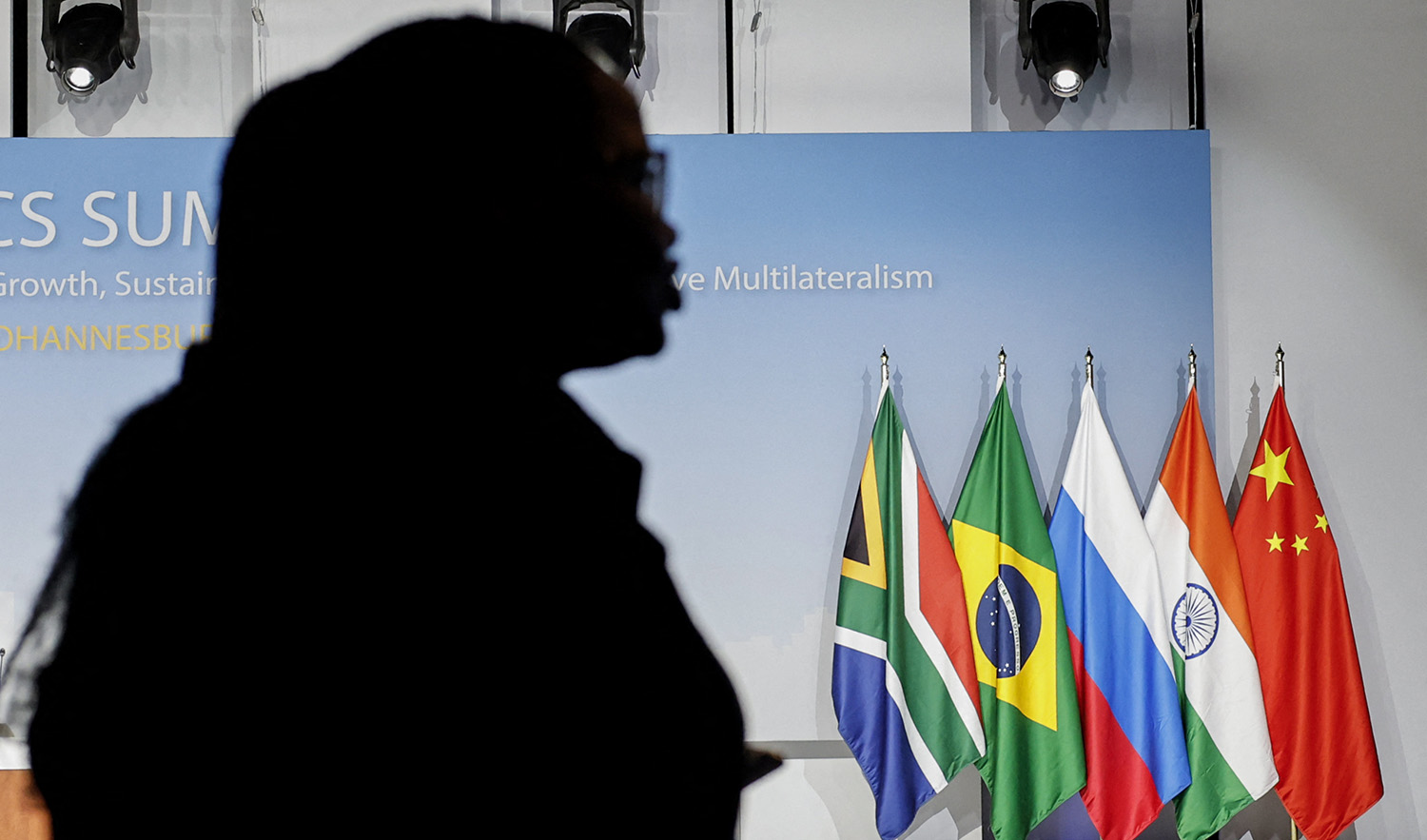 A woman stands near the flags of South Africa, Brazil, Russia, India and China during the 2023 BRICS Summit at the Sandton Convention Centre in Johannesburg on August 24, 2023. (AFP/File)