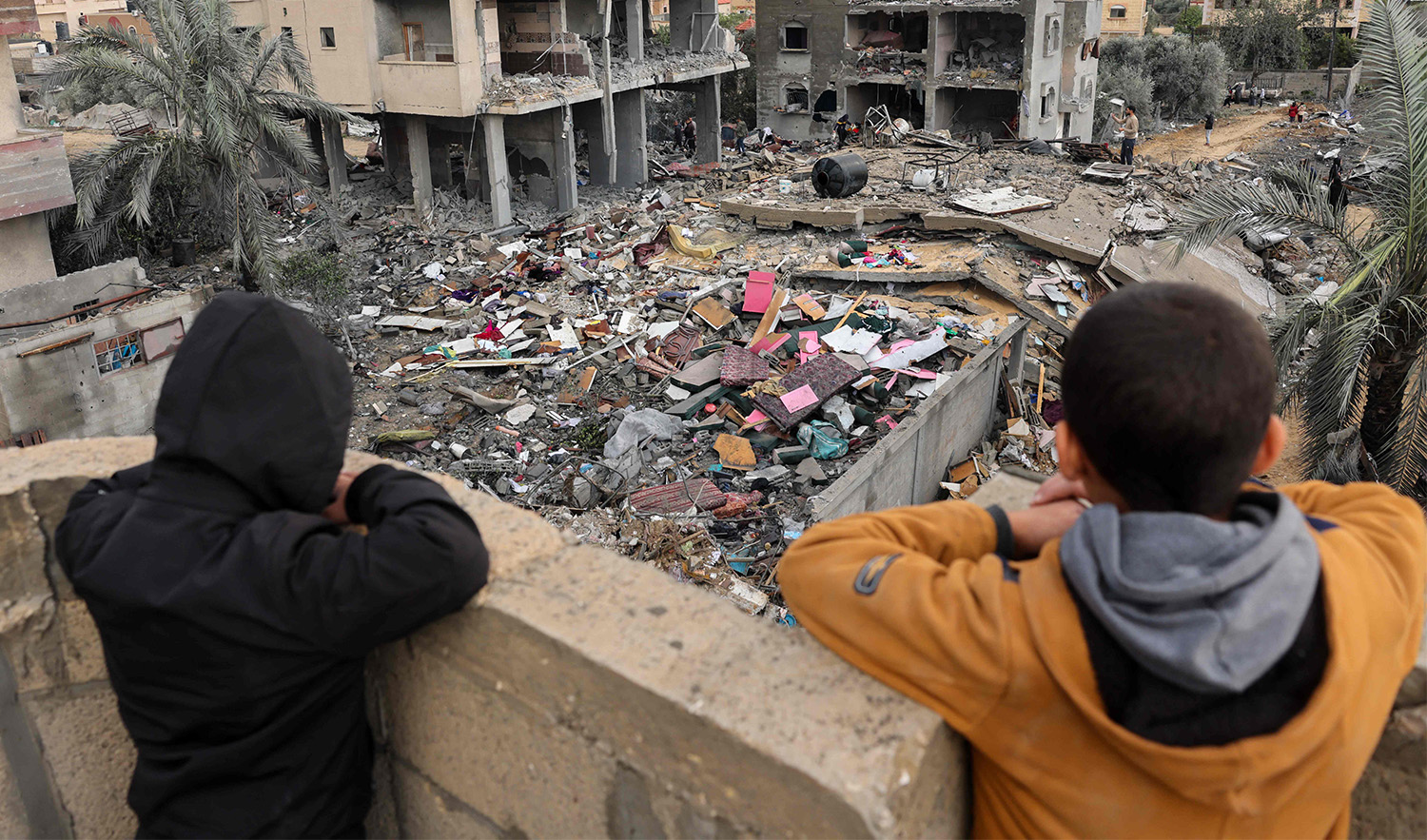 Palestinian children look on as people stand on the rubble of a building destroyed during Israeli strikes on Rafah, on the southern Gaza Strip, on November 20, 2023. (AFP)