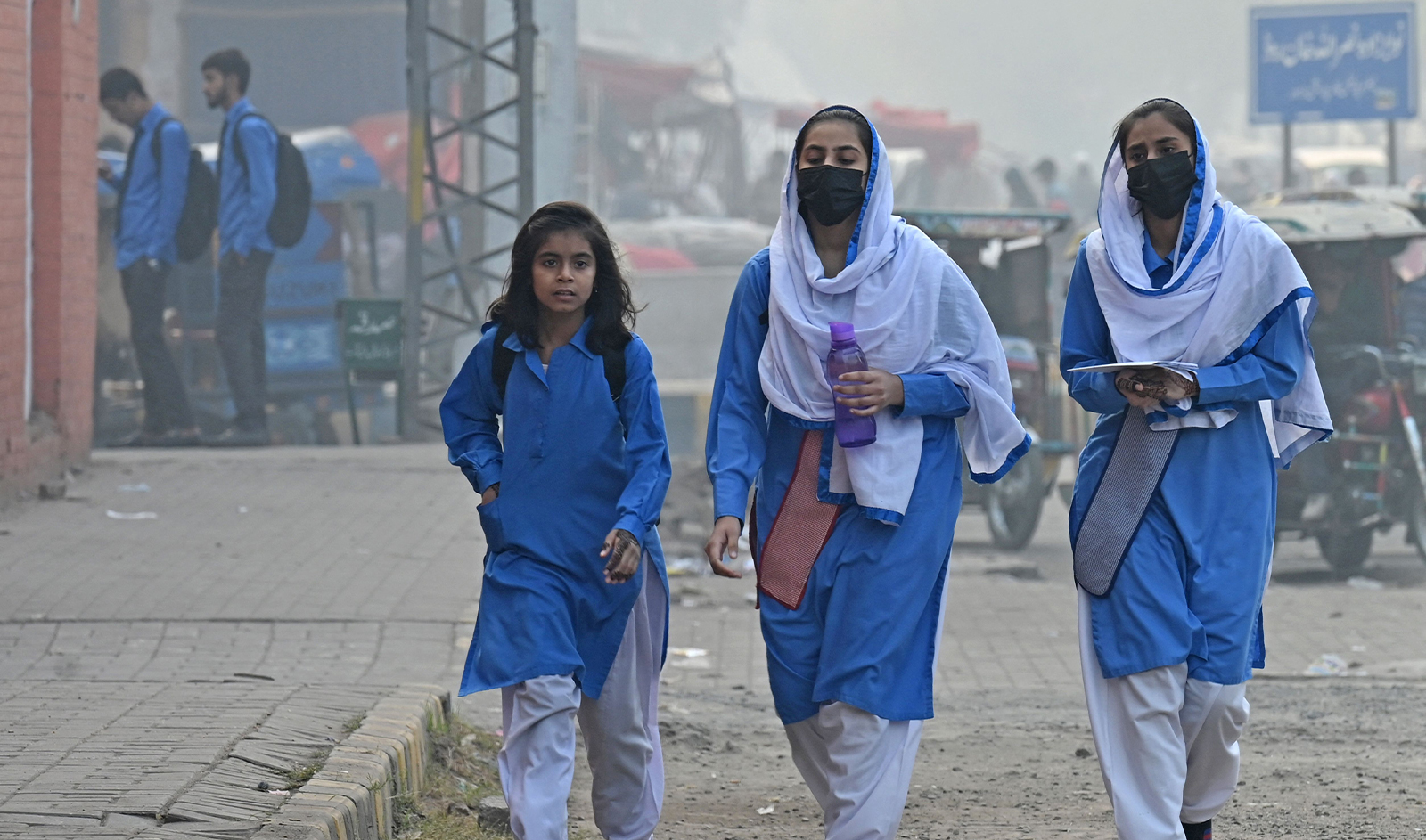 Students wearing face masks walk along a street amid smoggy conditions in Lahore, Pakistan on November 21, 2023. (AFP)