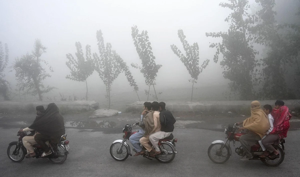 Men ride on bikes along a street amid smog conditions in Peshawar on November 11, 2023. (AFP)