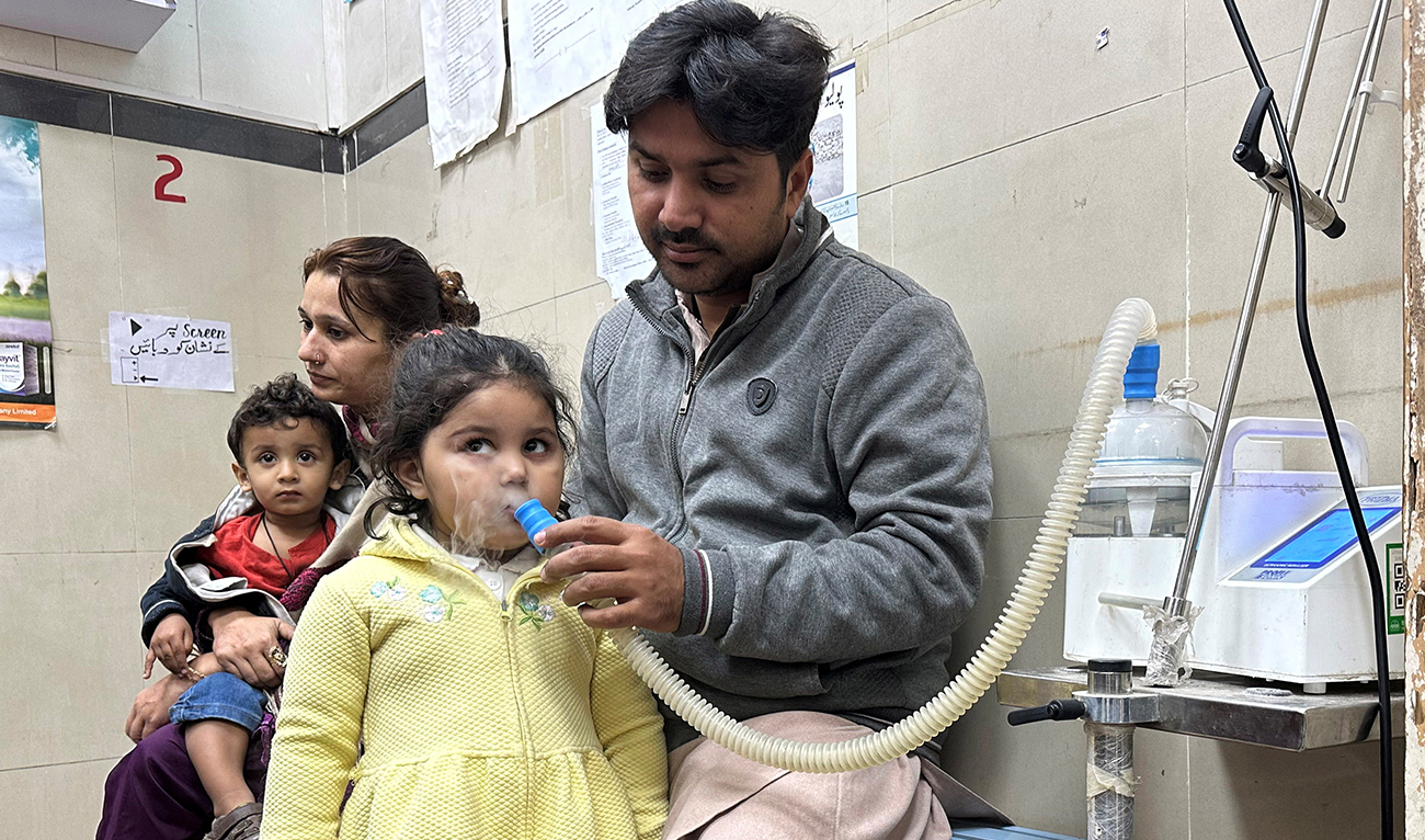 Mohamad Qadeer holds up a nebulizer device to the face of his daughter, Rameen, 3, who is suffering from a chest infection amidst soaring air pollution, in the emergency room of Sir Ganga Ram hospital in Lahore, Pakistan, December 4, 2023. (Reuters)