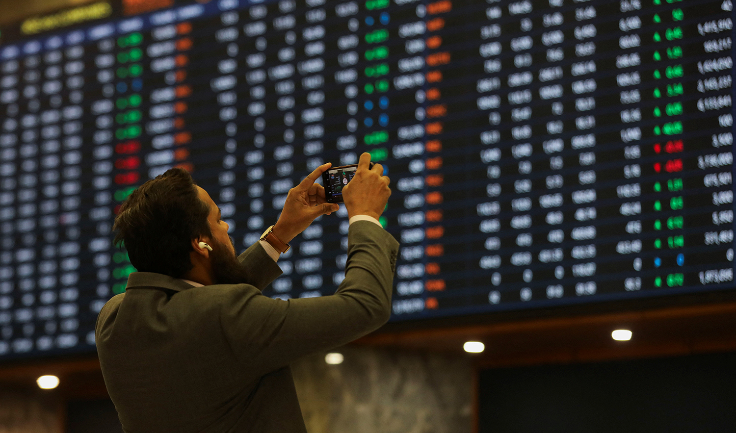 A man uses a mobile phone as he takes a photo of the electronic board displaying share prices during a trading session at the Pakistan Stock Exchange, in Karachi, Pakistan on November 28, 2023. (REUTERS/File)