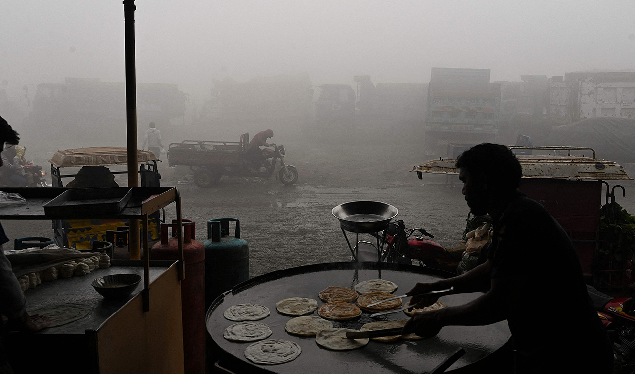 A worker makes bread along a road amid heavy smog in Lahore on December 14, 2023. (AFP)