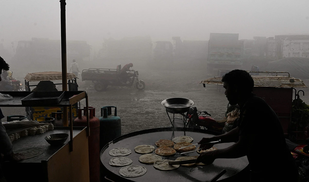 A worker makes bread along a road amid heavy smog in Lahore on December 14, 2023. (AFP)
