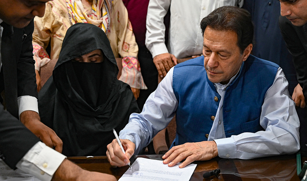 Pakistan's former Prime Minister, Imran Khan (R) along with his wife Bushra Bibi (C) signs surety bonds for bail in various cases, at a registrar office in the High court, in Lahore on July 17, 2023. (AFP/File)