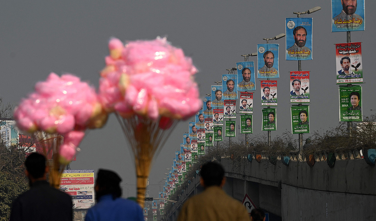 Candy sellers walk past the election campaign posters ahead of the upcoming general elections in Rawalpindi on January 9, 2024. (AFP)