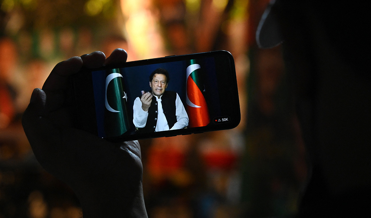An activist of Tehreek-e-Insaf (PTI) party listens to Pakistan's former Prime Minister Imran Khan's speech on a phone, in Zaman Park in Lahore on May 13, 2023. (AFP/File)