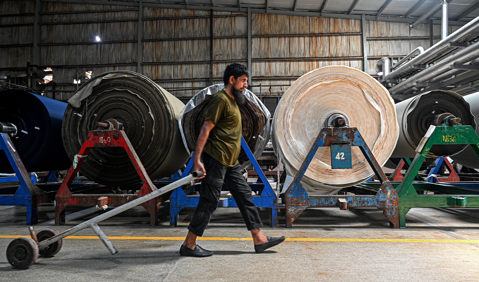 In this picture taken on July 20, 2023, a worker walks past fabric rolls at the Kohinoor Textile Mills in Lahore. (AFP/File)