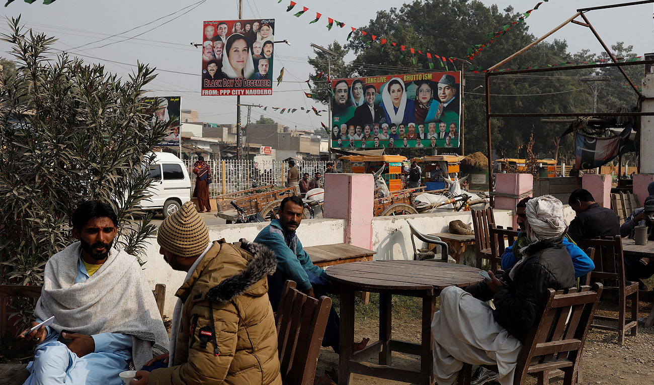 People sit outside a tea stall with billboards of political leaders in the background, ahead of the general elections in Larkana, Pakistan, January 16, 2024. (REUTERS)