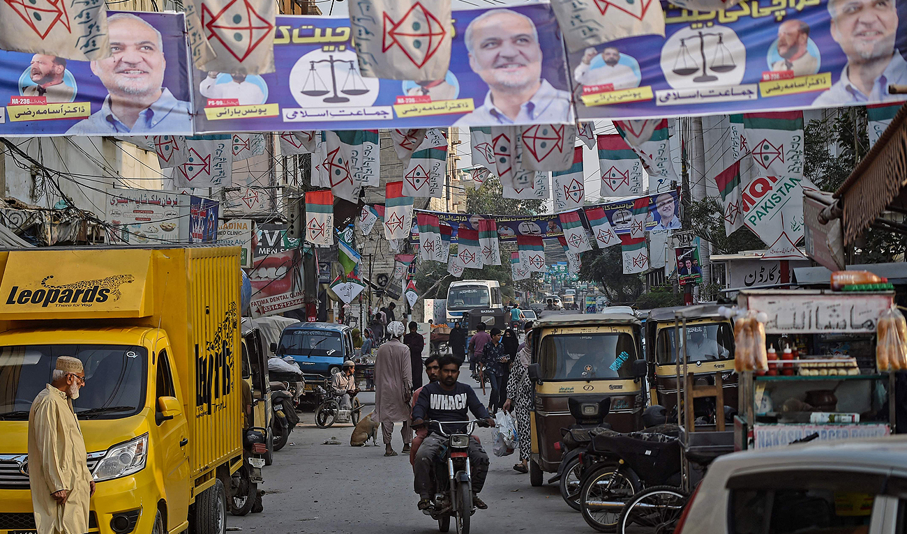 Commuters move past the election banners of Muttahida Qaumi Movement-Pakistan (MQM-P) and Jamaat-e-Islami (JI) parties hung over a street ahead of the upcoming general elections, in Karachi on January 24, 2024. (AFP)