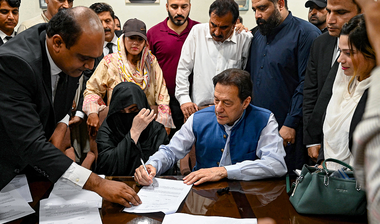 In this file photo, taken on July 17, 2023, Pakistan's former Prime Minister, Imran Khan (C) along with his wife Bushra Bibi (C, left) signs surety bonds for bail in various cases, at a registrar office in the High court, in Lahore. (AFP/File)