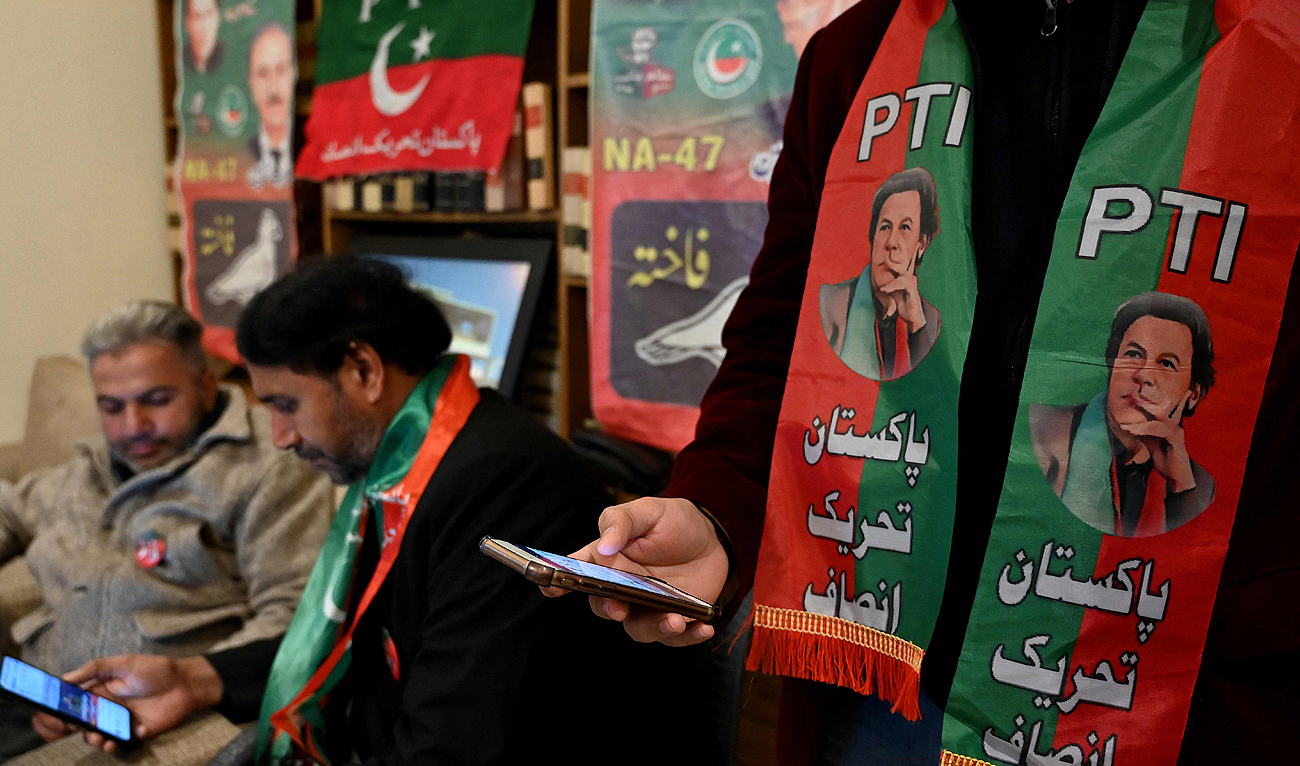 Pakistan's former prime minister Imran Khan's supporters wear scarves with prints of his Pakistan Tehreek-e-Insaf (PTI) party as they listen to a virtual election campaign on phones at Khan's PTI office in Islamabad on February 3, 2024. (AFP)
