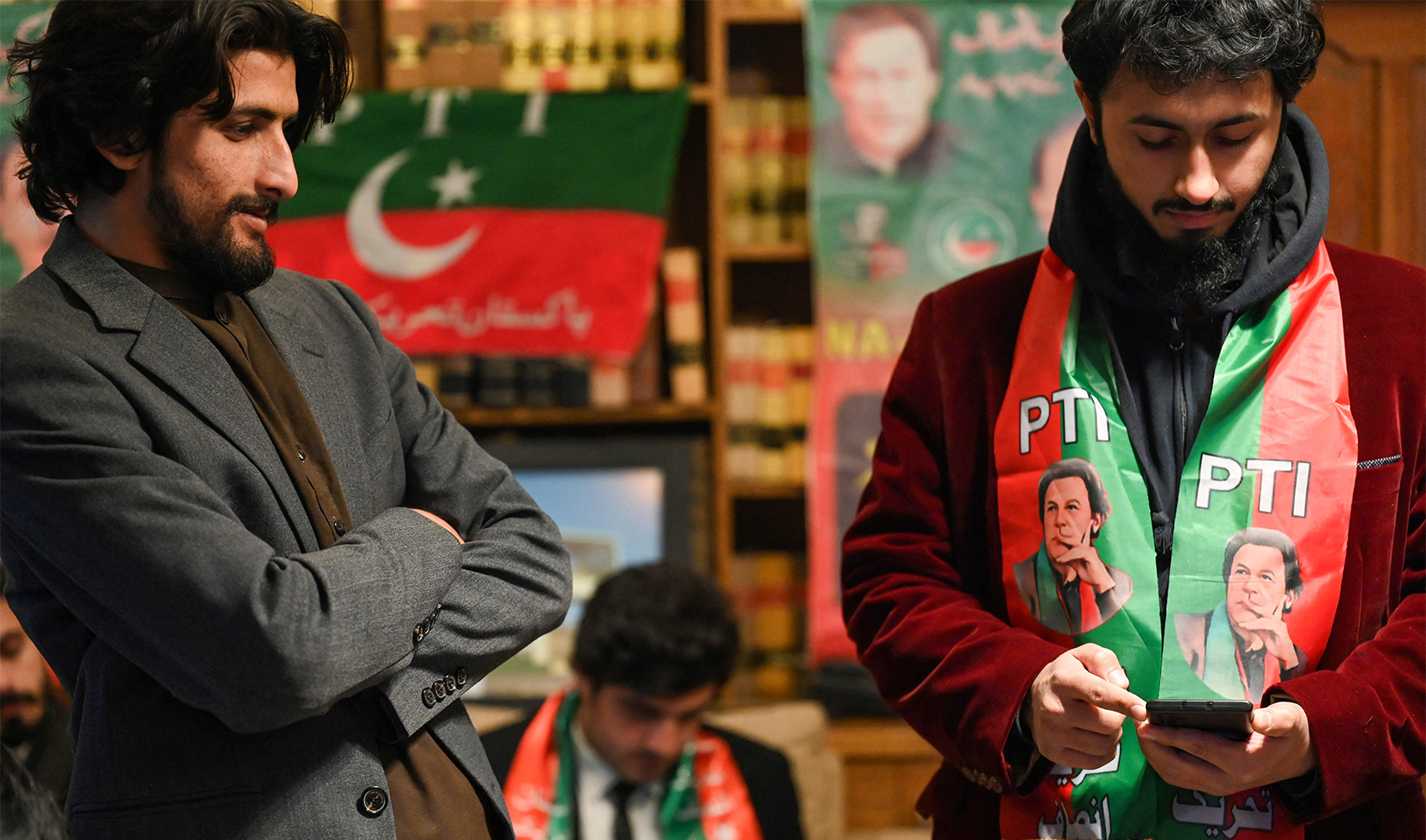 Pakistan's former prime minister Imran Khan's supporters wear scarves with prints of his Pakistan Tehreek-e-Insaf (PTI) party as they listen to a virtual election campaign on phones at Khan's PTI office in Islamabad on February 3, 2024. (AFP/File)