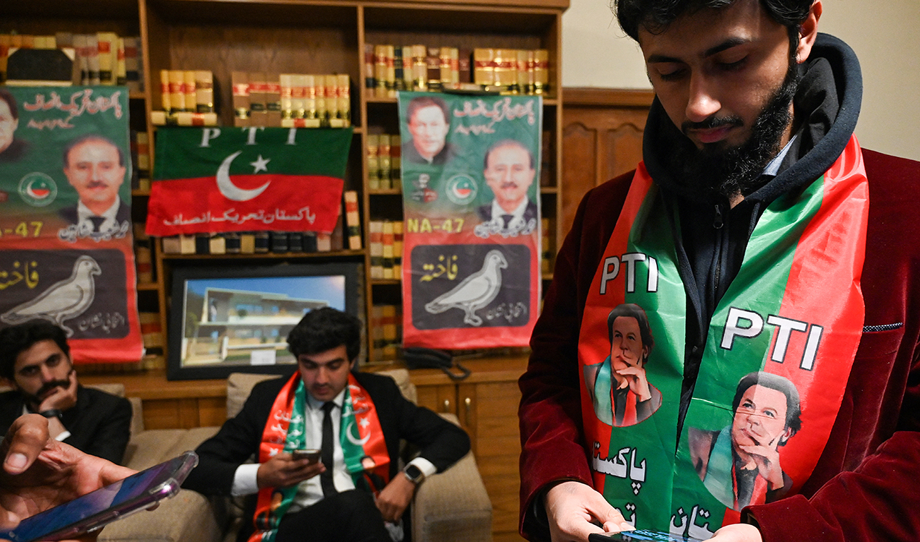 Pakistan's former prime minister Imran Khan's supporters wear scarves with prints of his Pakistan Tehreek-e-Insaf (PTI) party as they listen to a virtual election campaign on phones at Khan's PTI office in Islamabad on February 3, 2024. (AFP/File)
