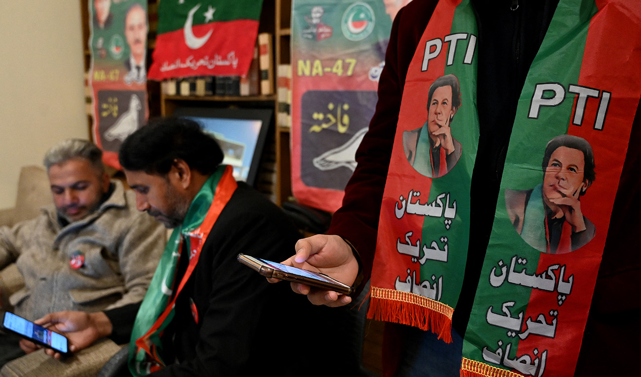 Pakistan's former prime minister Imran Khan's supporters wear scarves with prints of his Pakistan Tehreek-e-Insaf (PTI) party as they listen to a virtual election campaign on phones at Khan's PTI office in Islamabad on February 3, 2024. (AFP/File)