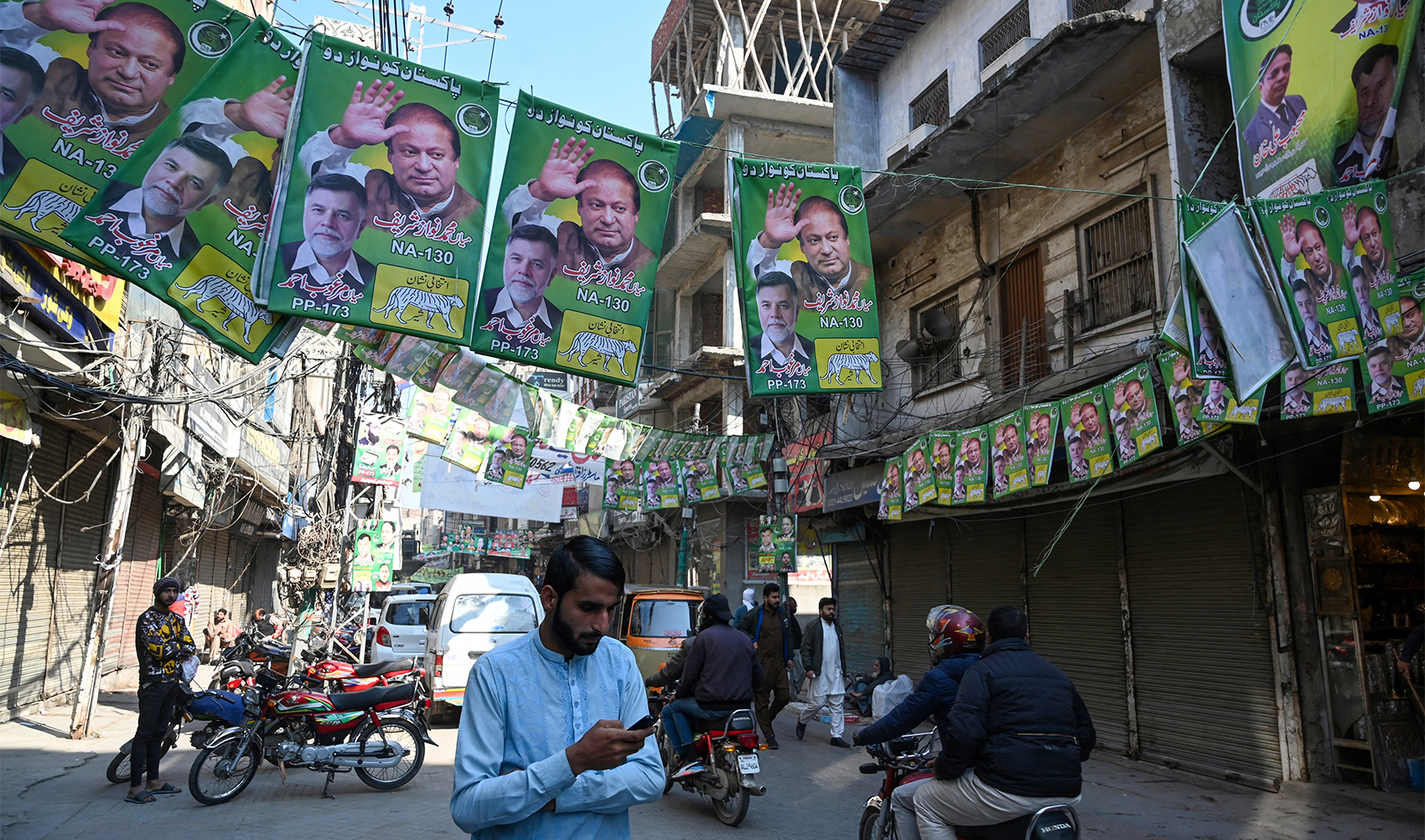 Commuters ride past posters of Nawaz Sharif Pakistan's former Prime Minister and leader of the Pakistan Muslim League (PML) party, a day after national elections in Lahore on February 9, 2024. (AFP)