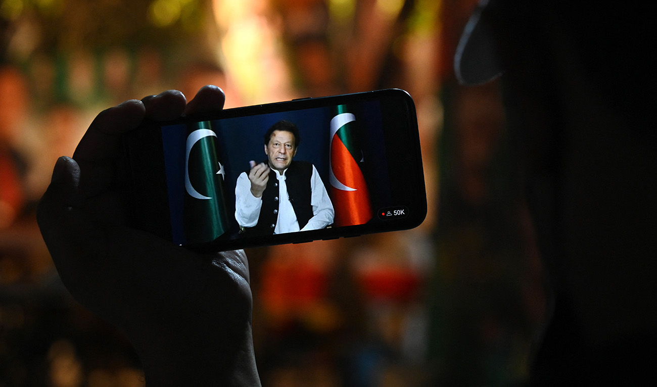 An activist of Tehreek-e-Insaf (PTI) party listens to Pakistan's former Prime Minister Imran Khan's speech on a phone, in Zaman Park in Lahore on May 13, 2023. (AFP/File)