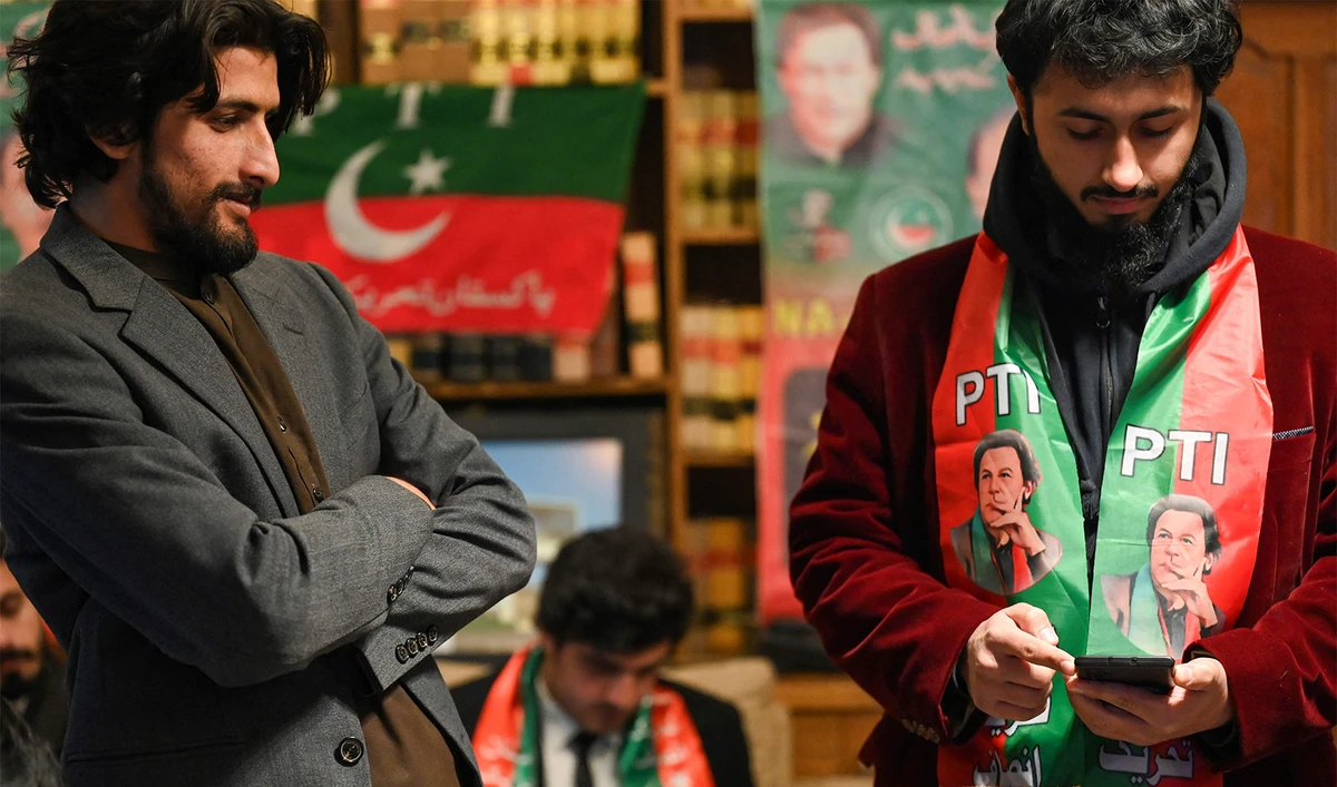 Pakistan's former prime minister Imran Khan's supporters wear scarves with prints of his Pakistan Tehreek-e-Insaf (PTI) party as they listen to a virtual election campaign on phones at Khan's PTI office in Islamabad on February 3, 2024. (AFP/File)
