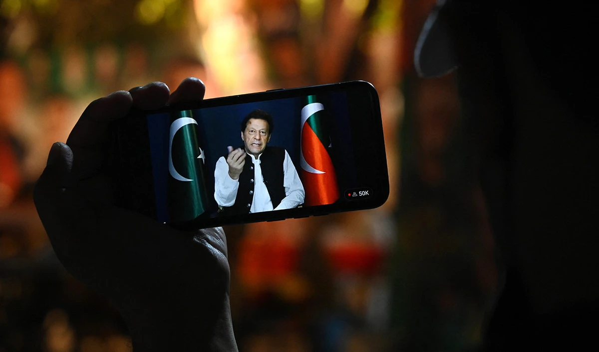 An activist of Tehreek-e-Insaf (PTI) party listens to Pakistan's former Prime Minister Imran Khan's speech on a phone, in Zaman Park in Lahore on May 13, 2023. (AFP/File)
