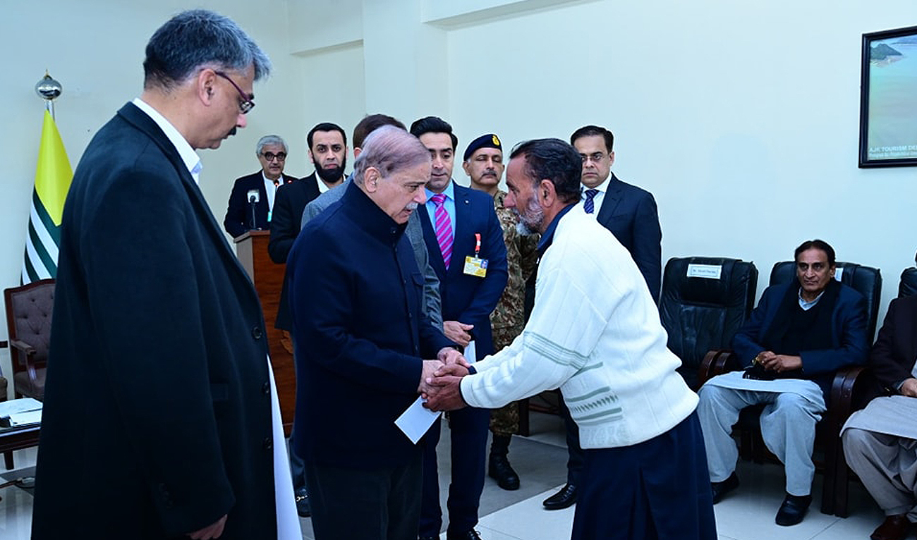 In this handout photo, taken and released by Prime Minister’s Office, Prime Minister Shehbaz Sharif interacts with a man while distributing assistance cheques to the families of the victims of recent torrential rains and heavy snowfall in Muzaffarabad, Azad Kashmir on March 8, 2024. (Photo courtesy: GOP)