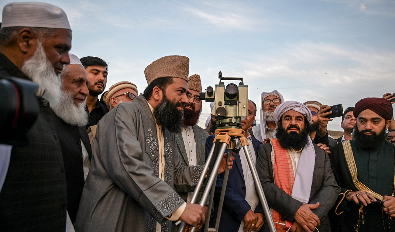 A Muslim scholar (5L) looks through a telescope for sighting of the new moon at sundown to mark the start of Islam's holy fasting month of Ramadan in Peshawar on March 11, 2024. (AFP)