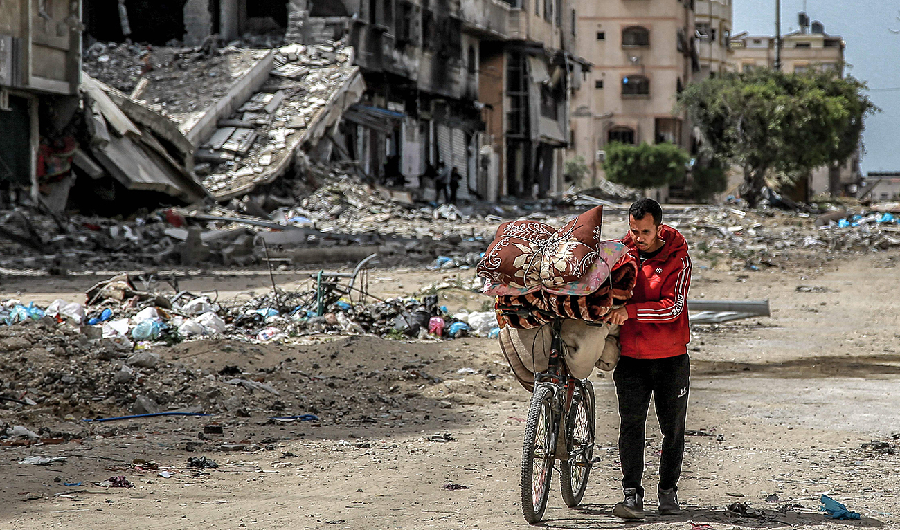A man walks with a bicycle loaded with blankets and cushions past destroyed buildings along a street in Gaza City on March 27, 2024 amid the ongoing conflict in the Gaza Strip between Israel and Hamas. (AFP)