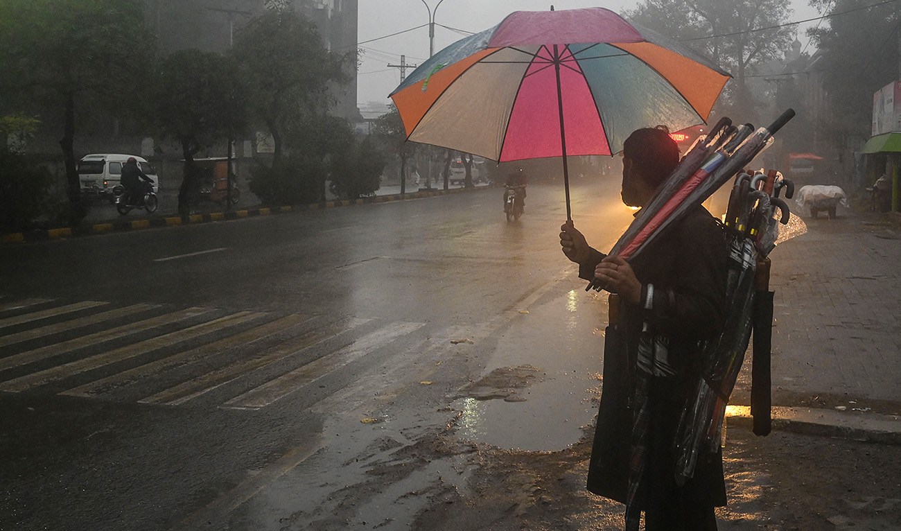A street vendor carries umbrellas as he waits for customers along a road during a rain shower in Lahore on January 19, 2022. (AFP/File)