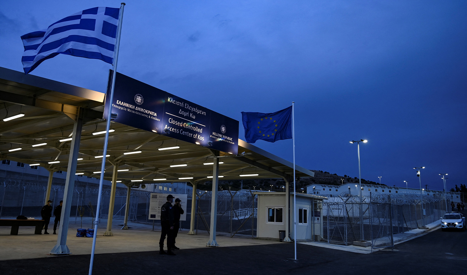 Employees stand at the entrance to the new closed migrant camp in the Greek island of Kos on November 27, 2021. (AFP)