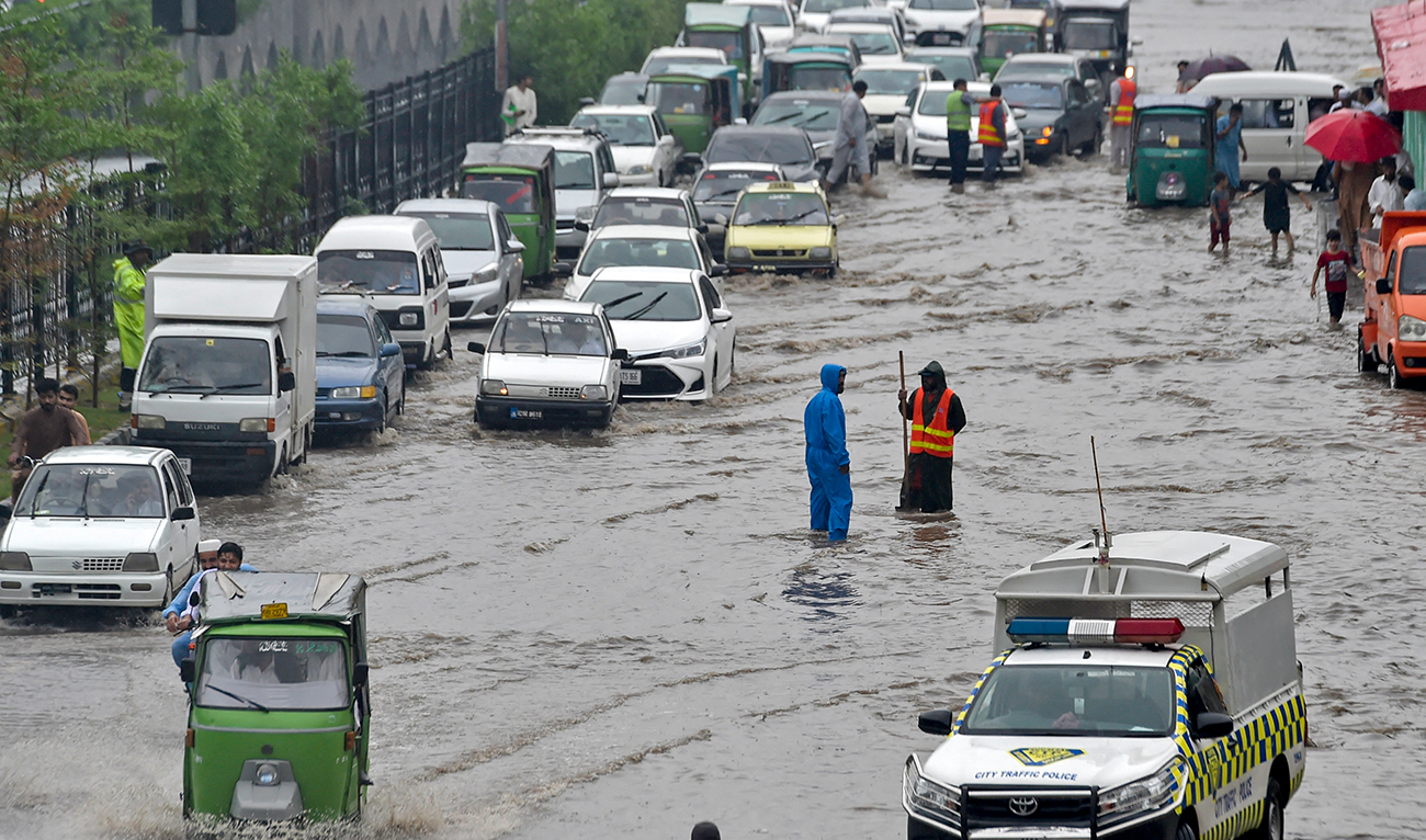 Commuters make their way through a flooded street after a heavy rain shower in Peshawar on August 17, 2022. (AFP/File)