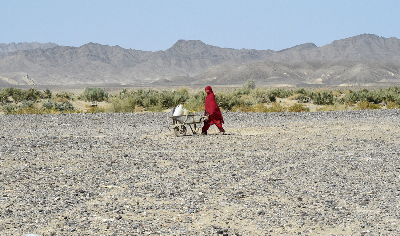 A woman carries water cans in a wheelbarrow at the Koh-e-Sabz area of Pakistan's south-west Baluchistan province where Iran launched an airstrike, on January 18, 2024. (AFP/File)