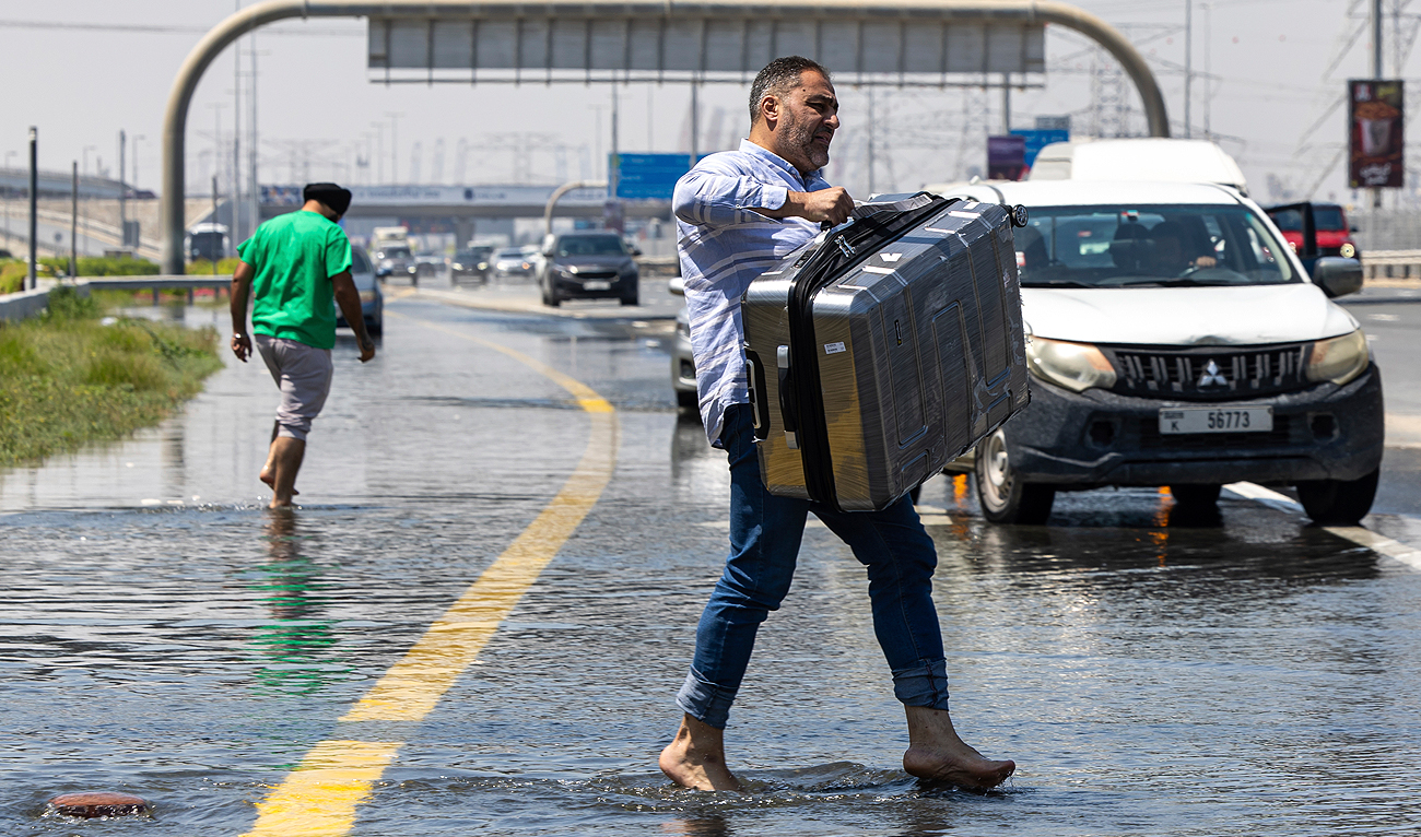 A man carries luggage through floodwater caused by heavy rain while waiting for transportation on Sheikh Zayed Road highway in Dubai, United Arab Emirates, Thursday, April 18, 2024. (AP)