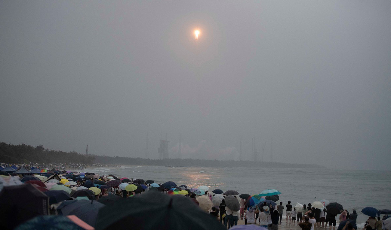 A crowd watches from a beach as a Long March 5 rocket, carrying the Chang’e-6 mission lunar probe, lifts off as it rains at the Wenchang Space Launch Center in southern China’s Hainan Province on May 3, 2024. (AFP)
