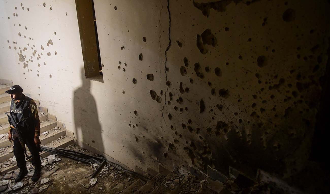 A police officer stands next to a bullet-riddled wall as he inspects a police compound after taking control of the building, following an attack by Pakistani Taliban, in Karachi on February 17, 2023. (AFP/File)