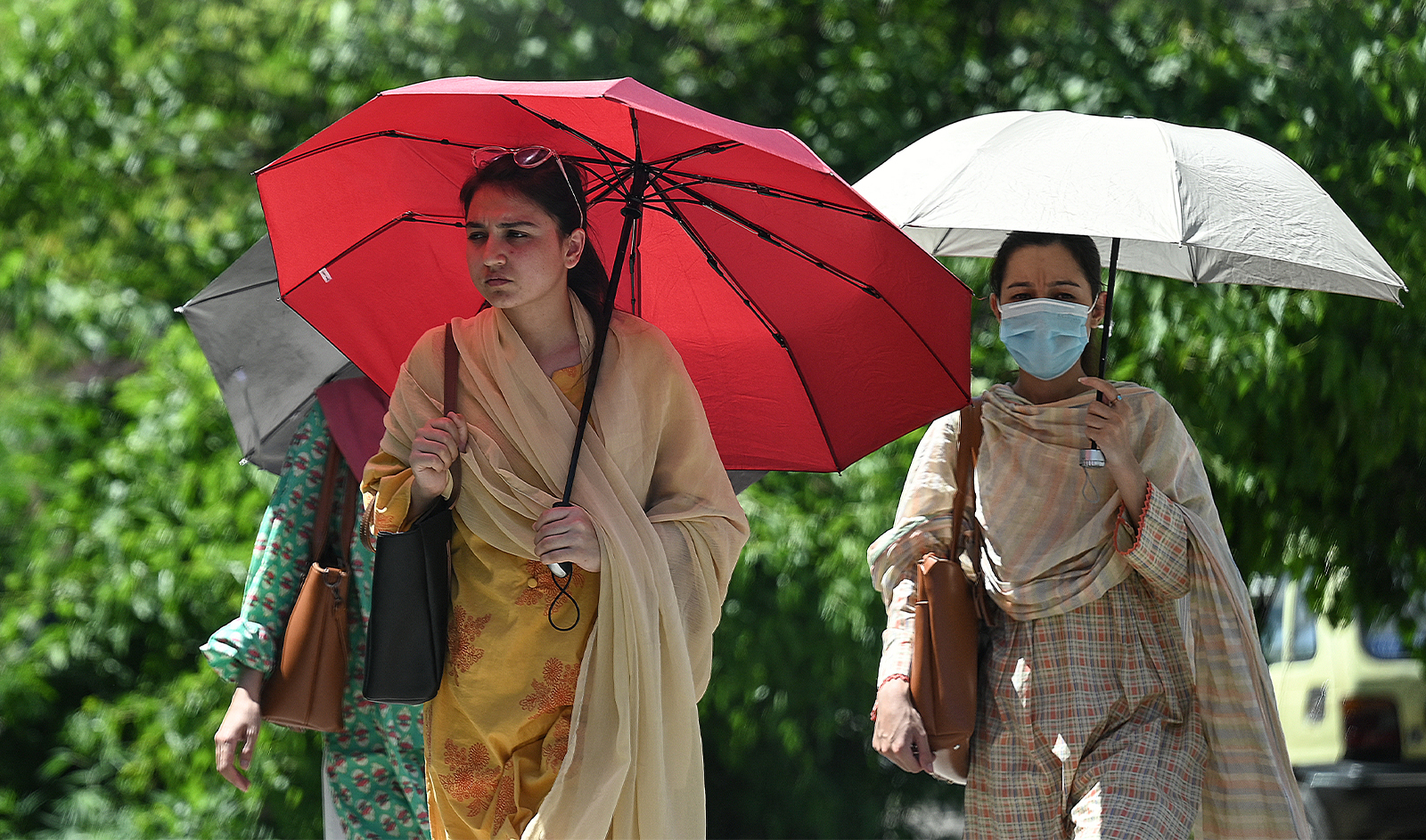 Women shelter from the sun under umbrellas as they walk along a street during hot summer day in Islamabad on May 8, 2024. (AFP)