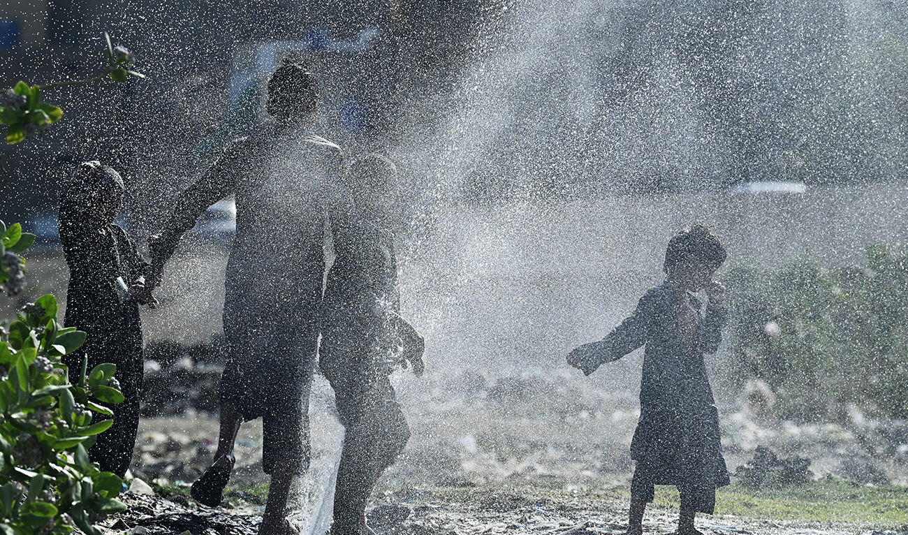 Youths cool off as water bursts out from a damaged water pipe line amidst a heatwave in Karachi on May 21, 2024. (AFP)