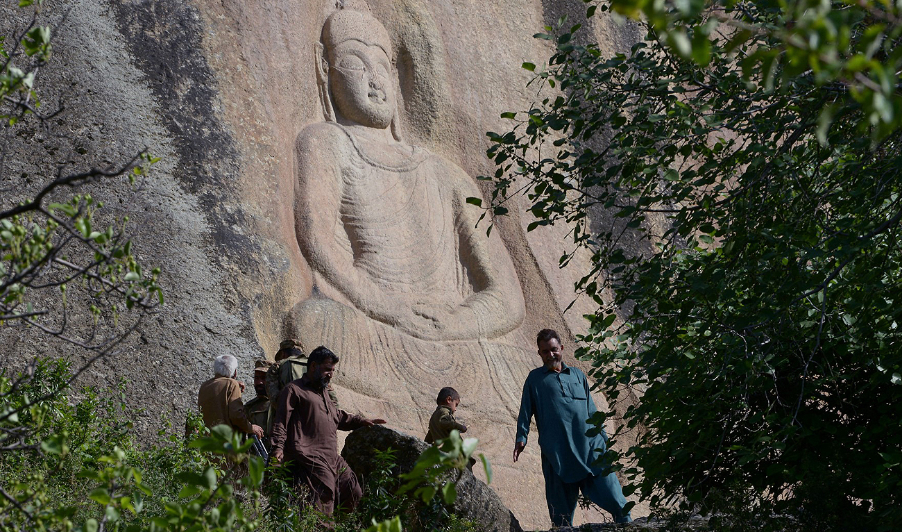 This photo taken on April 26, 2018 shows Pakistani visitors walking past the seventh-century rock sculpture of a seated Buddha carved into a mountain in Jahanabad town in the northwestern Swat Valley of Pakistan. (AFP/File)