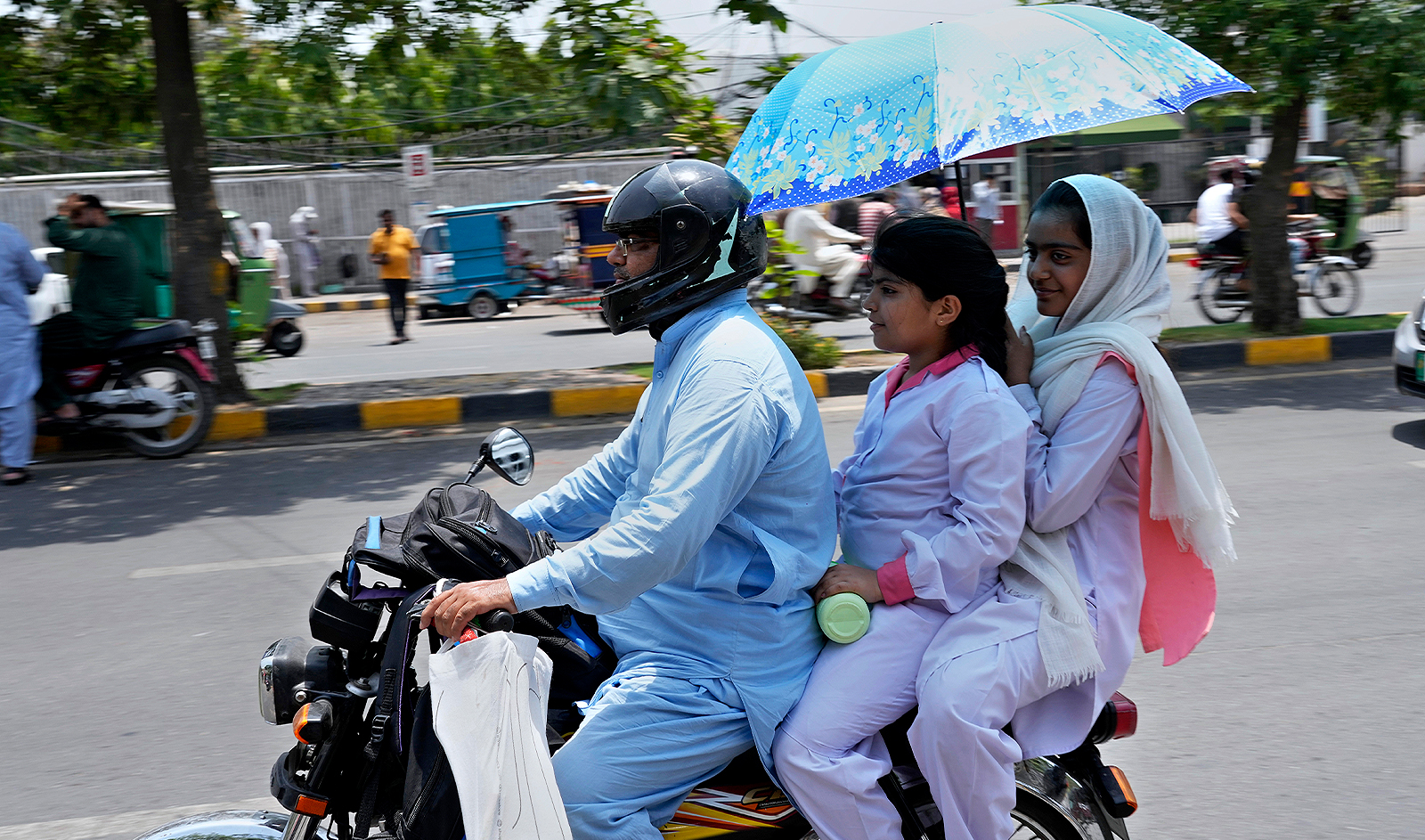 Students use an umbrella to protect themselves from heat as they travel on a bike after attending their school, in Lahore, Pakistan, on May 21, 2024. (AP)