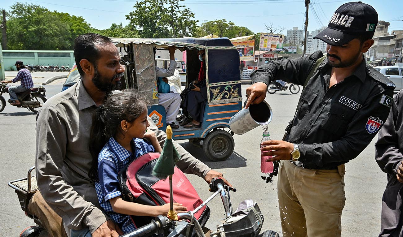 A policeman distribute cold drinks to bypassers near a 'heatwave relief camp' during a hot summer day in Karachi on May 23, 2024. (AFP)