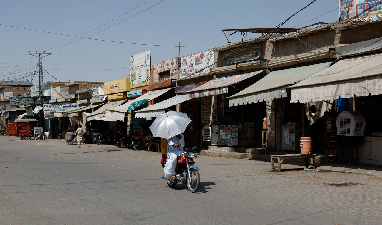 A couple rides on a motorbike carrying an umbrella to avoid sunlight, along a deserted market during a hot summer day as the heatwave continues in Jacobabad, Pakistan May 26, 2024. (REUTERS)