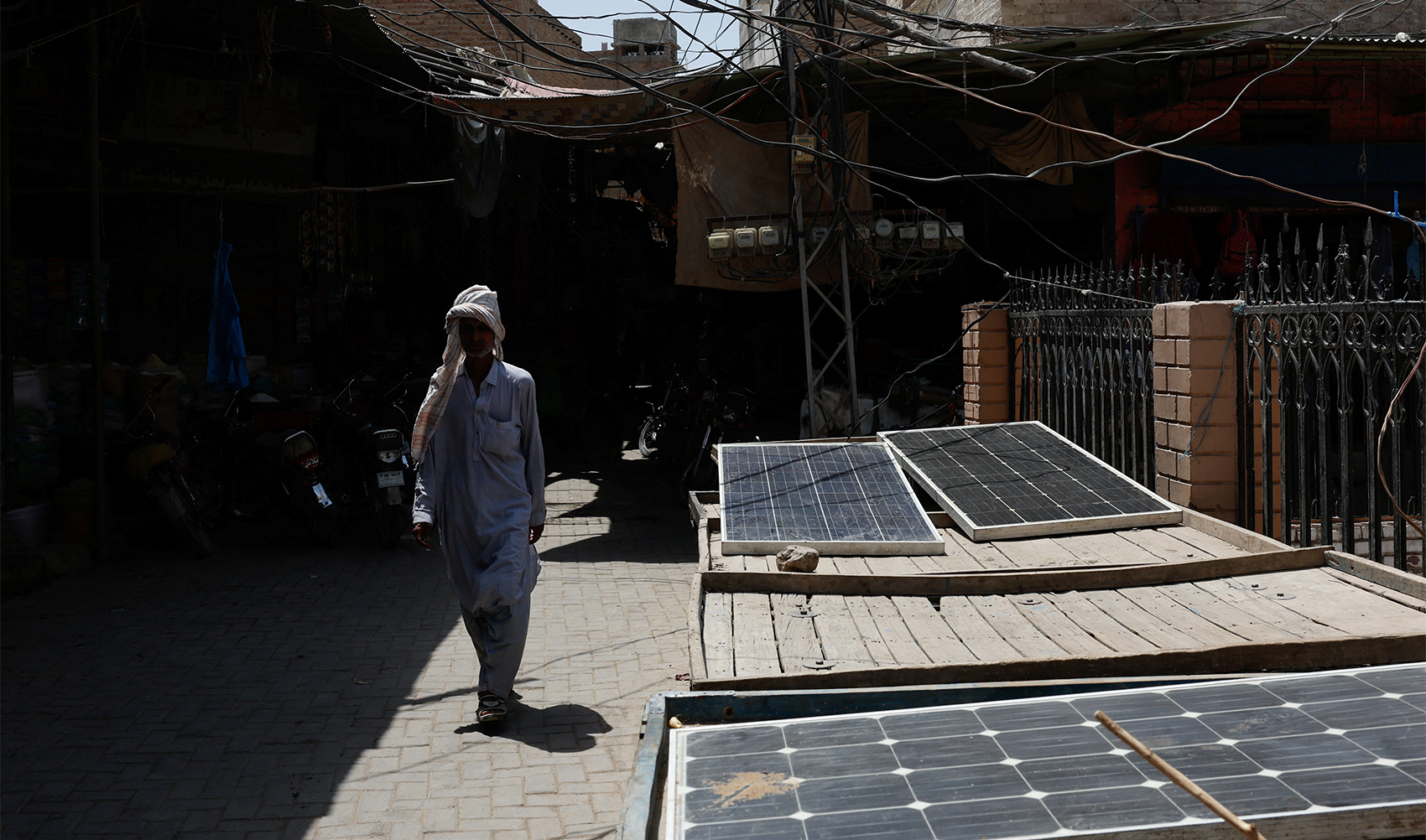 A man with his head covered with a scarf to avoid sunlight, walks past solar panels during a hot summer day, as the heatwave continues in Jacobabad, Pakistan May 26, 2024. (AFP)