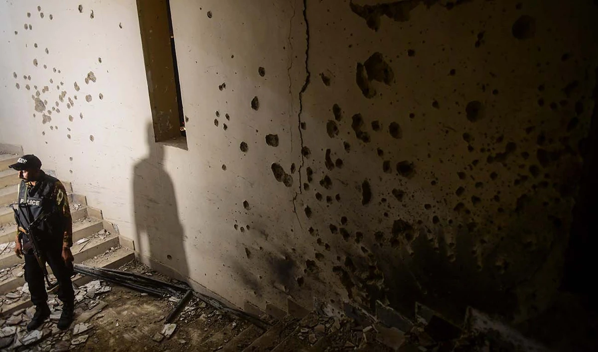 A police officer stands next to a bullet-riddled wall as he inspects a police compound after taking control of the building, following an attack by Pakistani Taliban, in Karachi on February 17, 2023. (AFP/File)