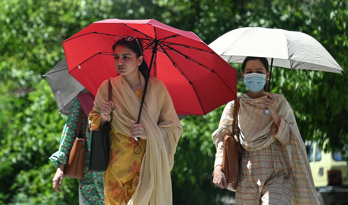 Women shelter from the sun under umbrellas as they walk along a street during hot summer day in Islamabad on May 8, 2024. (AFP)
