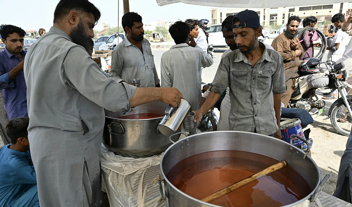 A volunteer distributes chilled soft drinks to bypassers along a street amidst a heatwave in Karachi on May 21, 2024. (AFP)