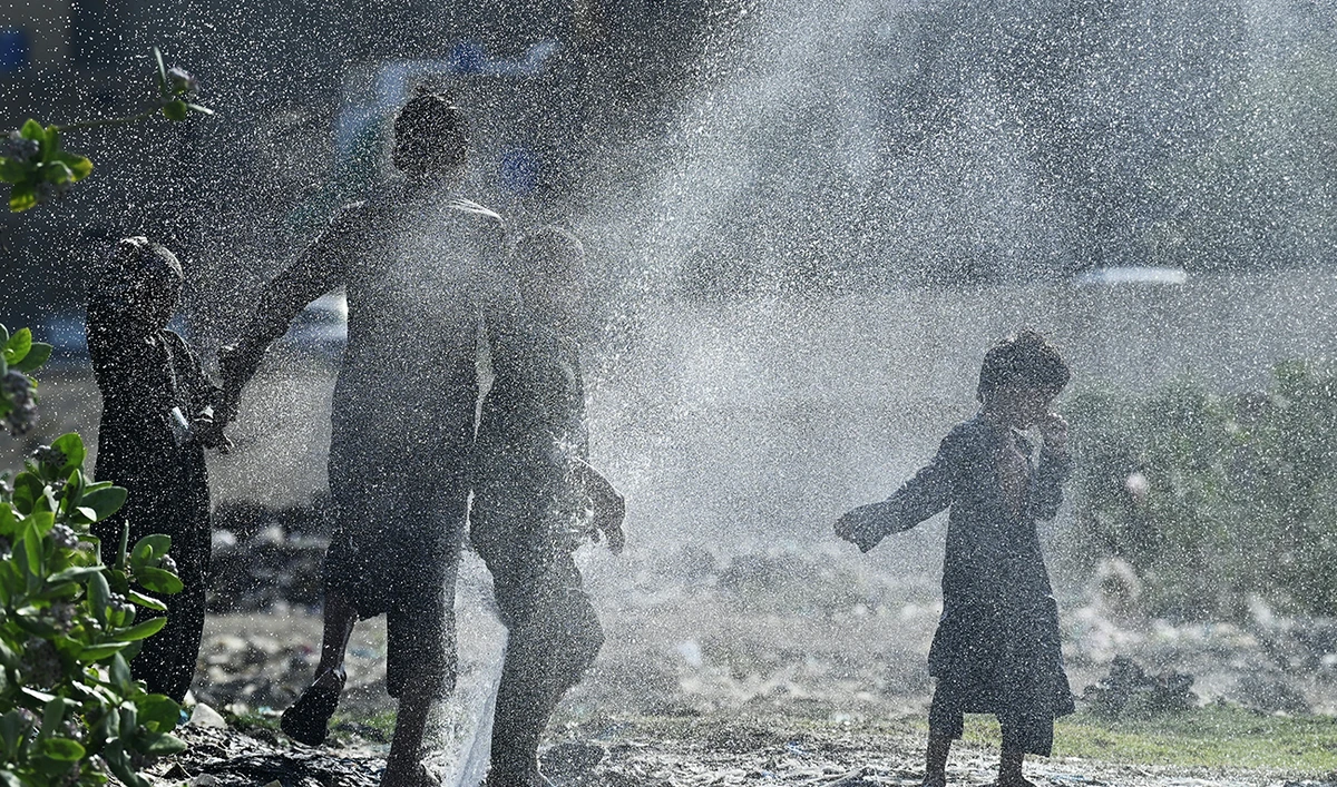 Youths cool off as water bursts out from a damaged water pipe line amidst a heatwave in Karachi on May 21, 2024. (AFP)