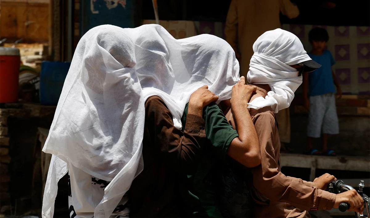 Men ride on a motorbike as they cover their heads with a wet cloth to cool off and to avoid sunlight, during a hot summer day, as the heatwave continues in Jacobabad, Pakistan on May 26, 2024. (REUTERS)